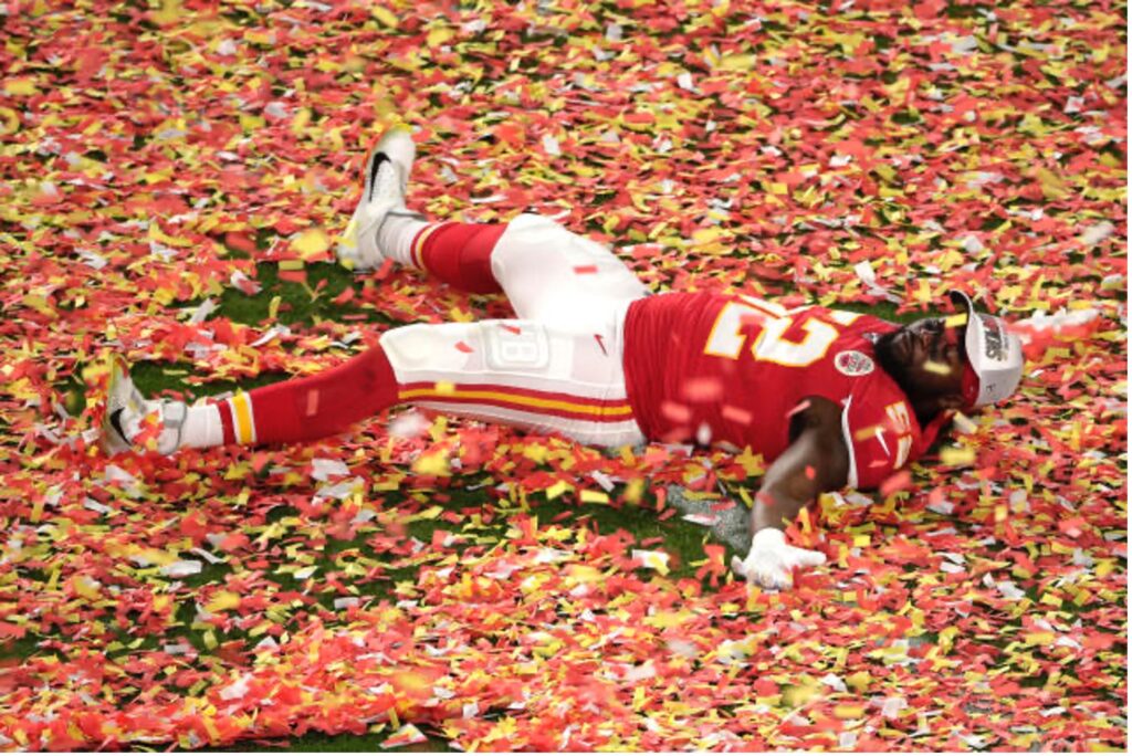 A Kansas City Chiefs player lies on the ground making a confetti angel in the red and yellow confetti that covered the field after the team won the 2024 Super Bowl.