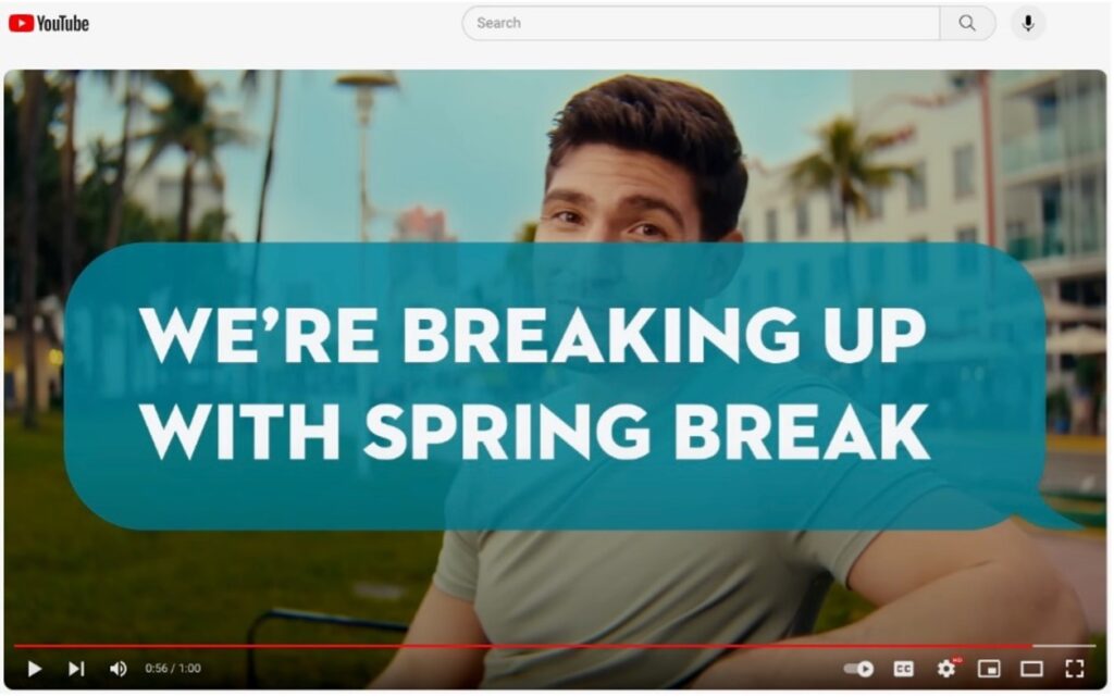 A still of a Youtube video from the city of Miami shows a young man with palm trees and the building behind him and the worlds "We're breaking up with spring break" displayed over him.